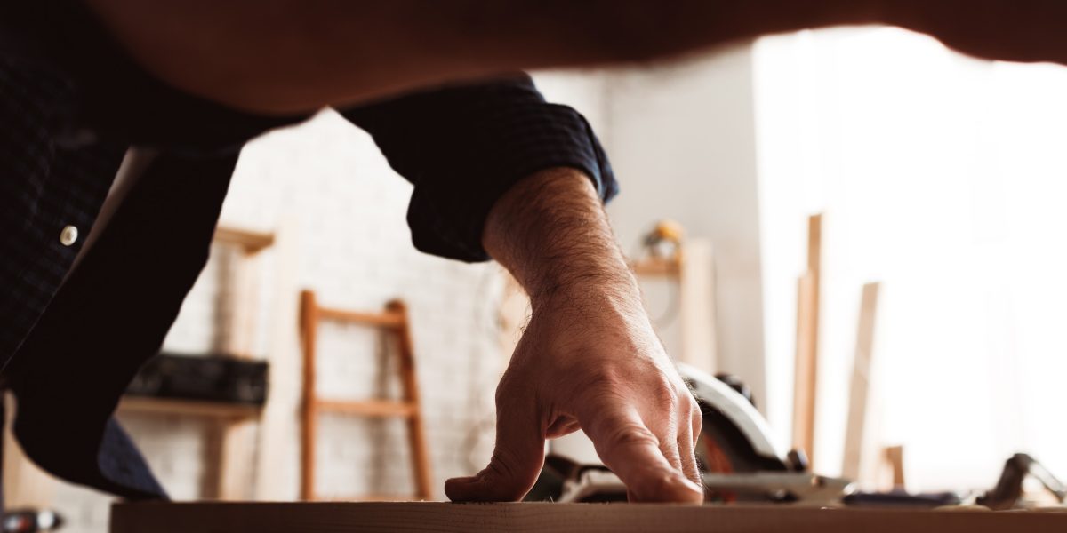 Male carpenter working with a wooden bar in a workshop close up